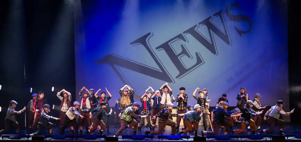 Newsies kneeling and pointing to the crowd