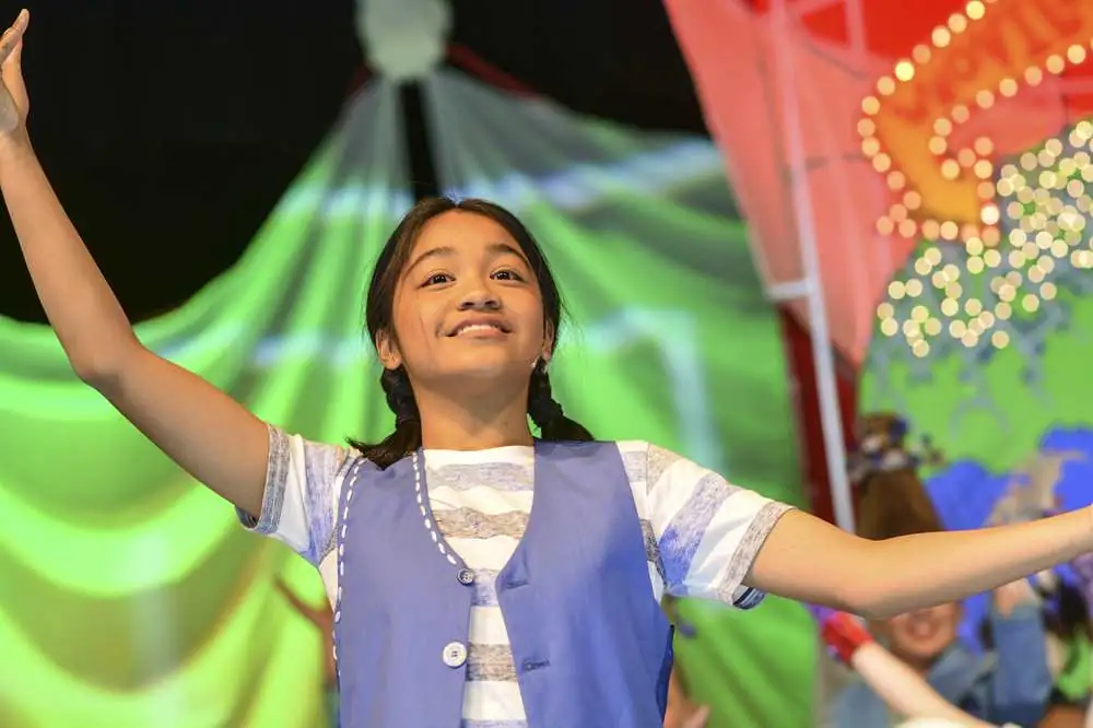 A young performer with arms out wide in a bright set