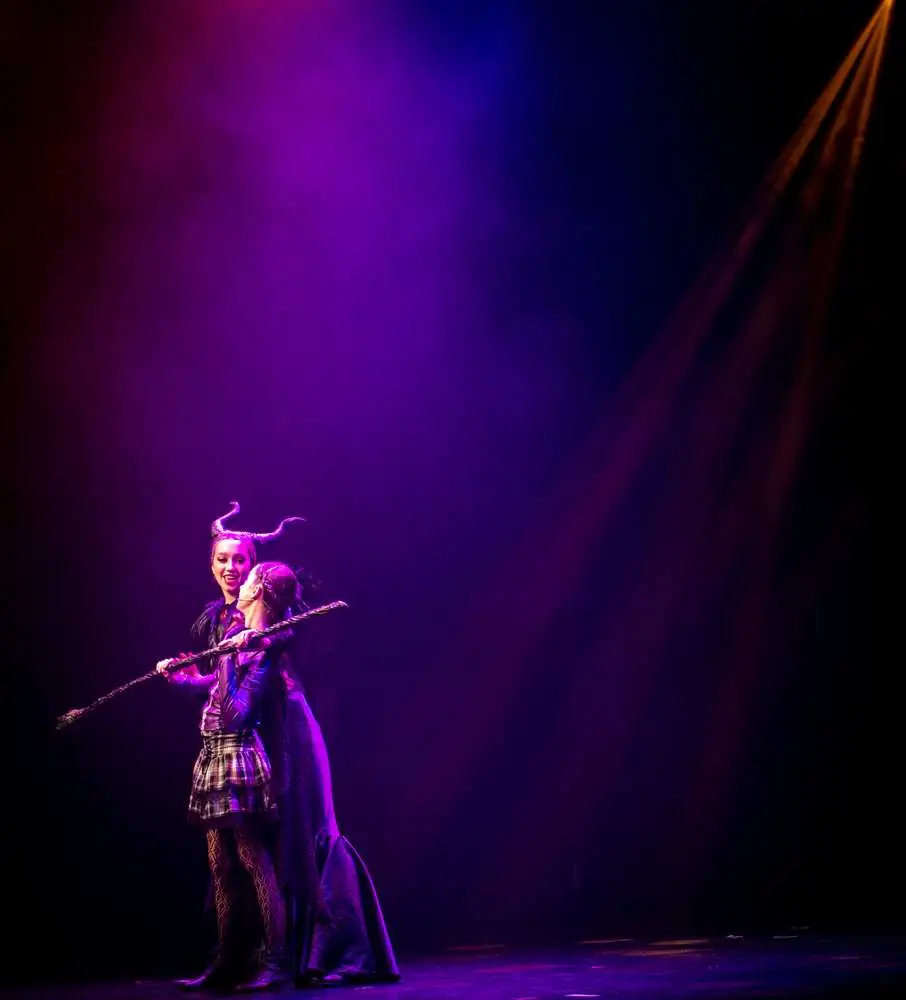A horned villain and a young performer in a purple spotlight