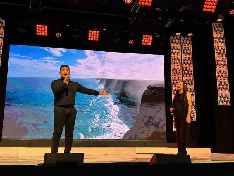 A singer on stage in front of ocean cliffs