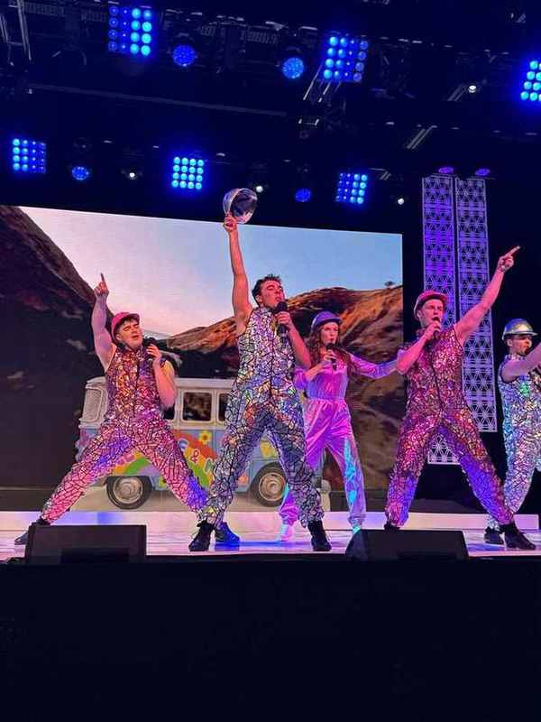 Performers in sequins and bold prints beside the road-trip van