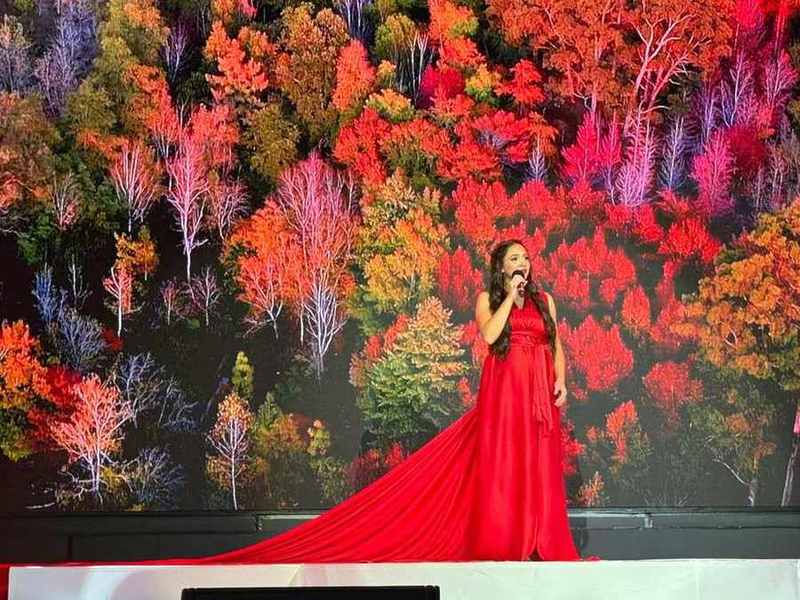 A soloist in a long red gown against autumn forest