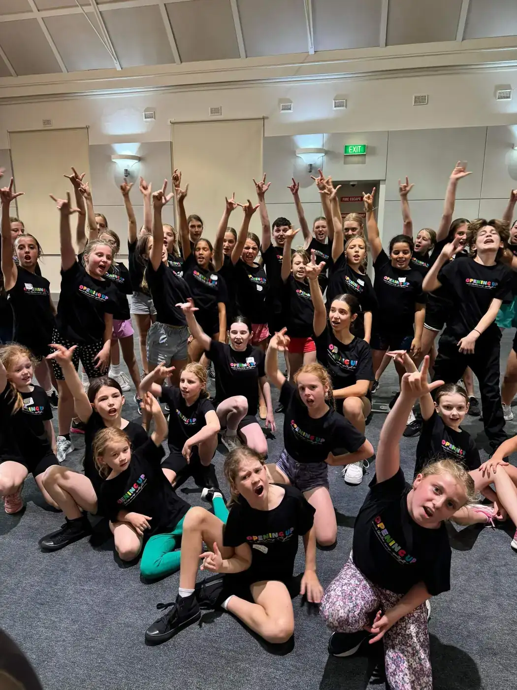 A big group of campers in matching black camp shirts with arms in the air