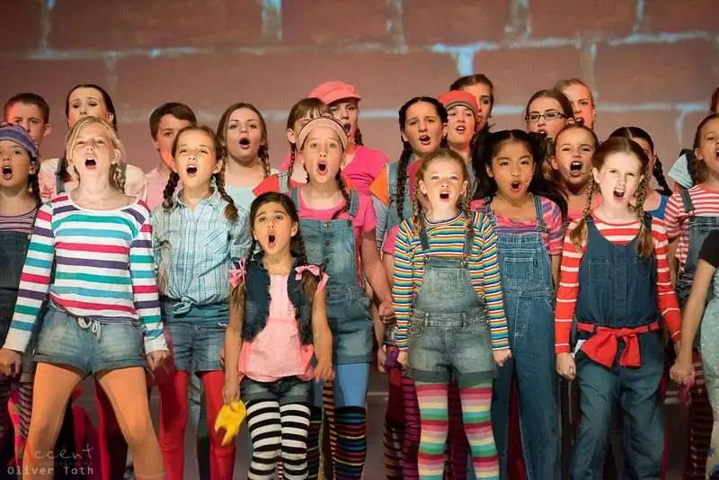 Young Pelican performers singing together in bright costumes